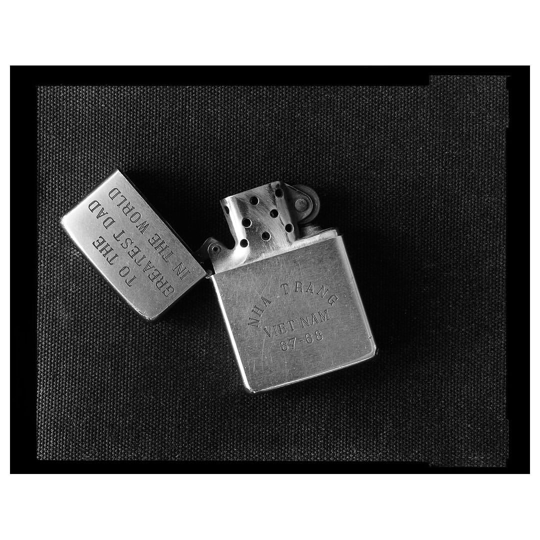 Black and white image of an open Zippo lighter with engraved text on a black surface, showcasing a vintage or personalized design.