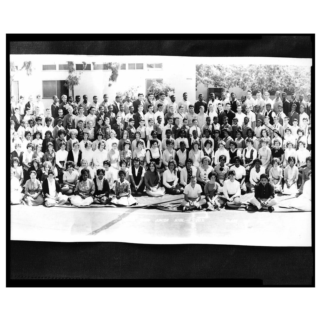 Large group of people gathered outdoors in a grayscale image, featuring a diverse crowd of adults posing for a group photograph.