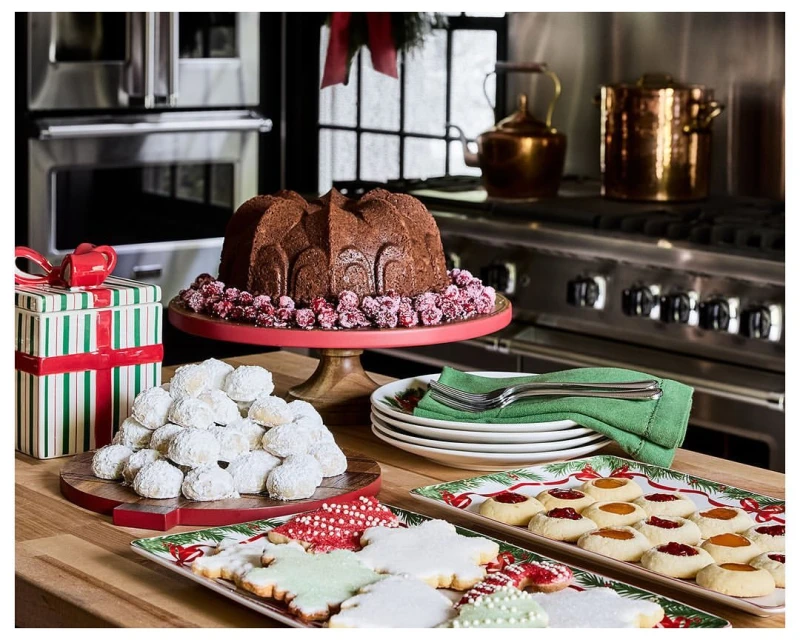 Holiday baking scene featuring a bundt cake, powdered sugar cookies, and decorated sugar cookies arranged on a wooden countertop.
