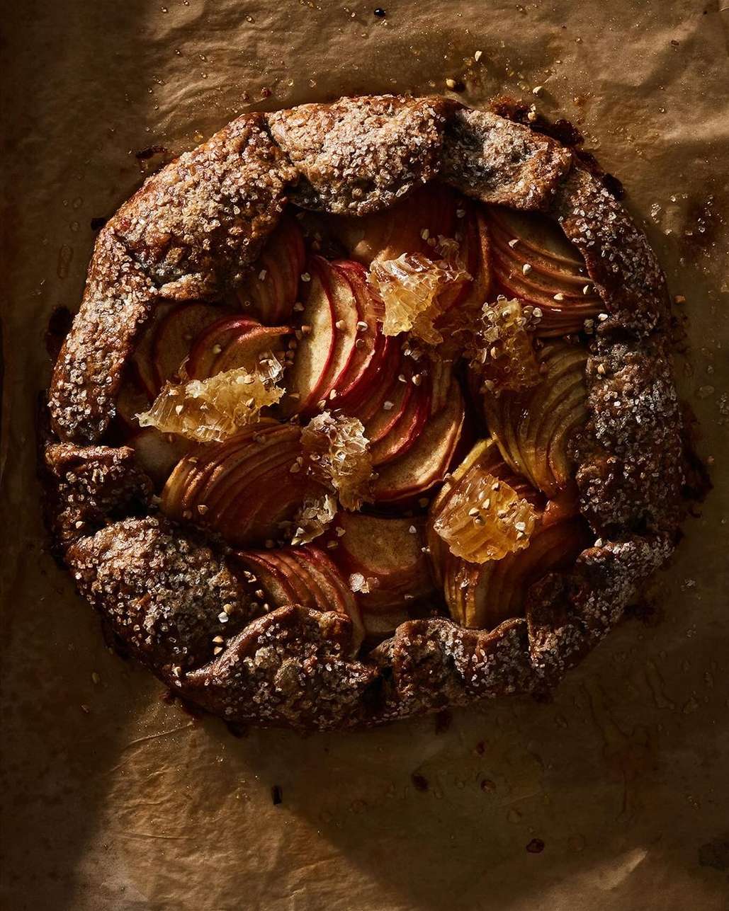 Overhead shot of a rustic apple galette on parchment paper, showcasing the golden-brown crust, sliced apples, and honey, ideal for food photography.