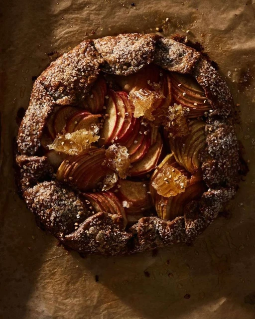 Overhead shot of a rustic apple galette on parchment paper, showcasing the golden-brown crust, sliced apples, and honey, ideal for food photography.