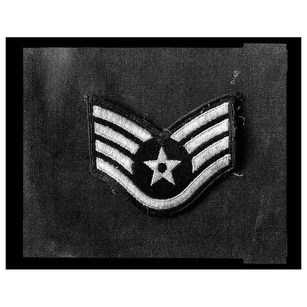 Military insignia patch featuring a star and stripes, attached to a dark fabric background, presented in black and white.