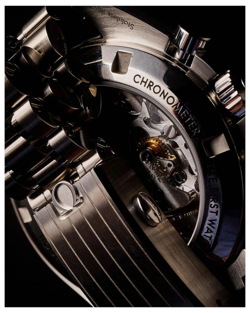 Macro shot of a stainless steel Chronometer watch with visible gears, showcasing intricate design and engineering on a dark background.