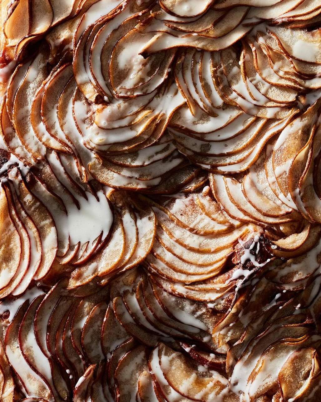 Overhead shot of a decorative apple tart, with thinly sliced apples arranged in concentric circles and topped with a creamy white glaze.