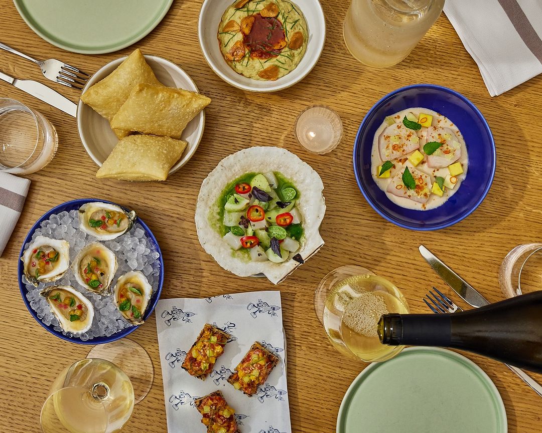 Overhead shot of an arrangement of various plates of food, glasses, and silverware on a wooden table, offering a vibrant culinary display.
