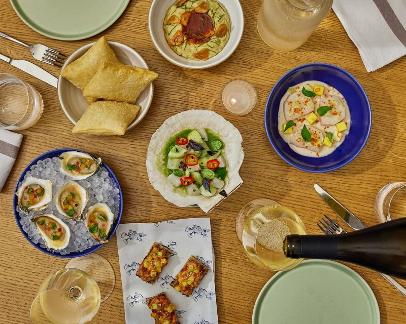 Overhead shot of an arrangement of various plates of food, glasses, and silverware on a wooden table, offering a vibrant culinary display.