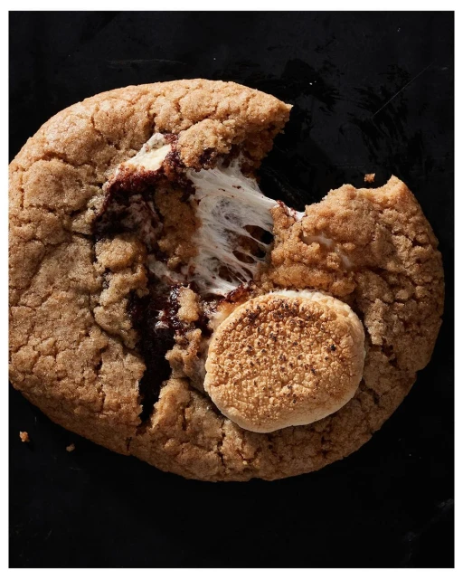 Overhead shot of a gooey, chocolatey s'mores cookie with toasted marshmallow on a dark background, tempting and delicious.