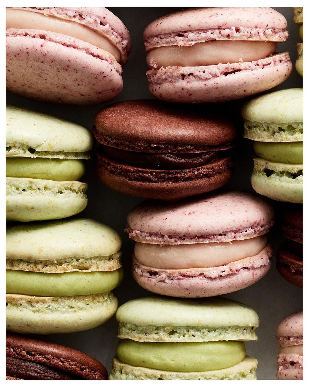 Overhead shot of stacked macarons in pink, brown, and green shades creating an appealing dessert food background, high-angle close-up view.