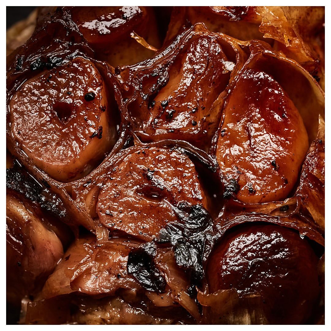 Close-up shot of roasted garlic bulbs with caramelized exteriors, displaying the cloves and dark brown, glazed appearance.