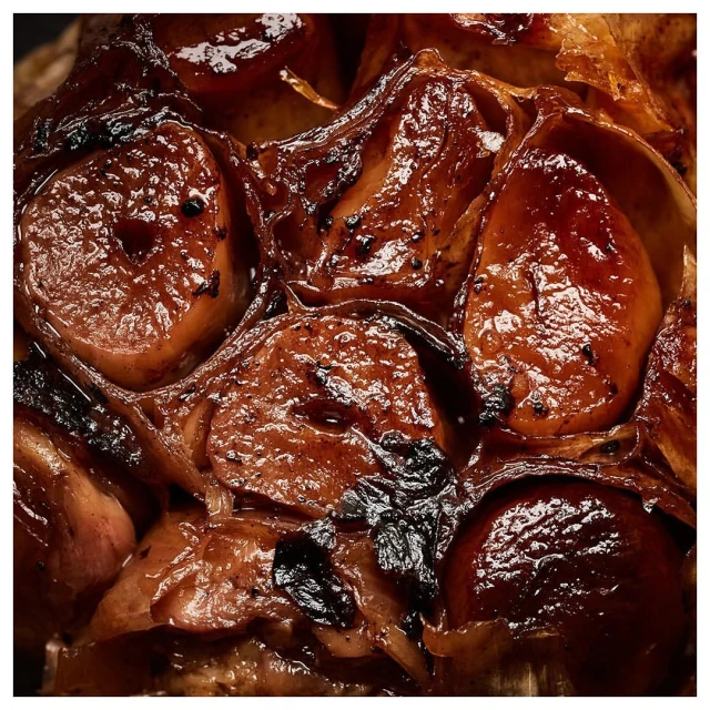 Close-up shot of roasted garlic bulbs with caramelized exteriors, displaying the cloves and dark brown, glazed appearance.