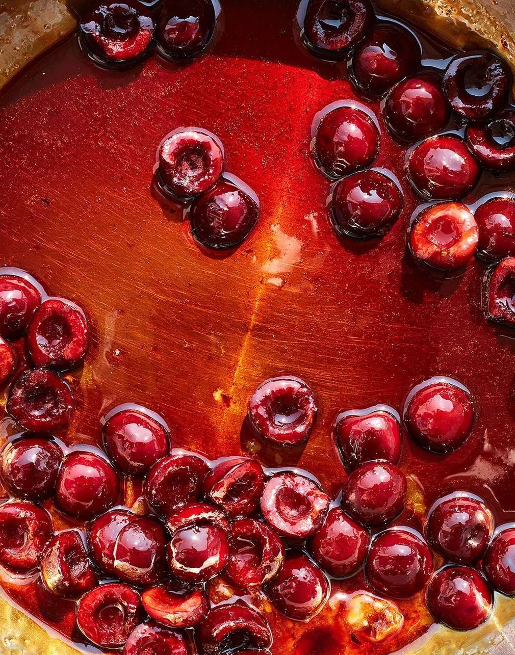 Close-up overhead shot of glistening cherries in a red liquid, showcasing their deep red color and juicy texture with a shallow depth of field.