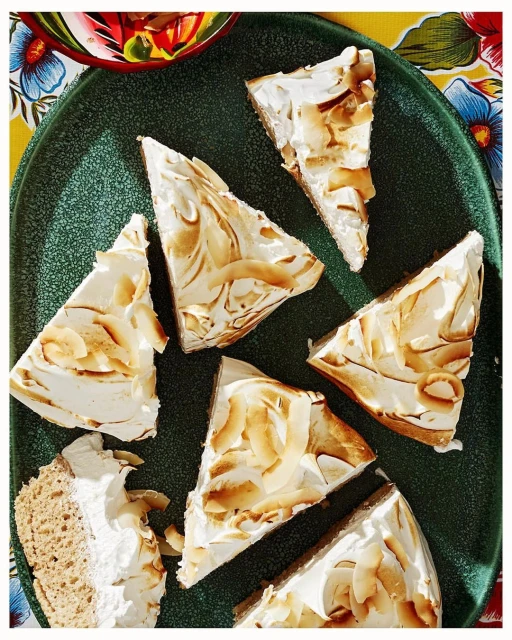 Overhead shot of multiple triangle slices of toasted coconut cream pie on a dark green serving platter with a colorful floral tablecloth.