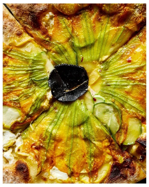 Overhead close-up of a vibrant pizza featuring fresh zucchini blossoms, delicate green zucchini slices, rich cheese, and black truffle.