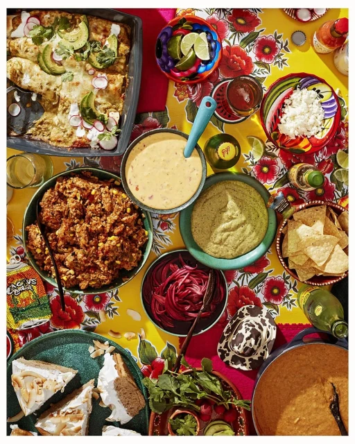 Overhead shot of a colorful table spread with Mexican food dishes, including enchiladas, shredded beef, sauces, toppings and tortilla chips.