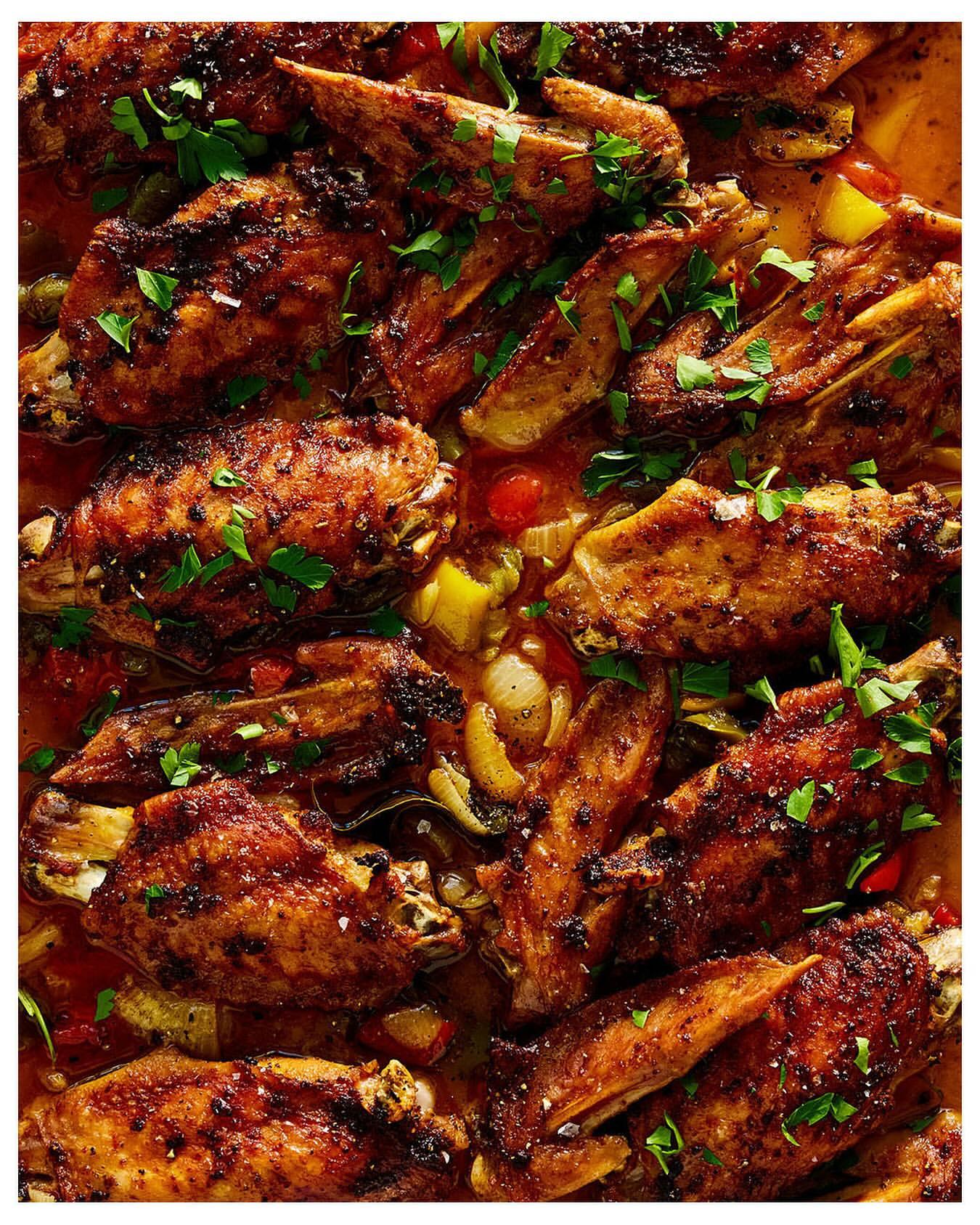 Overhead shot of sizzling, glazed chicken wings glistening with a rich, dark sauce, garnished with fresh herbs on a buffet line.