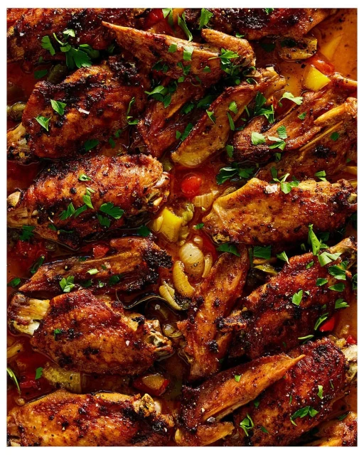 Overhead shot of sizzling, glazed chicken wings glistening with a rich, dark sauce, garnished with fresh herbs on a buffet line.