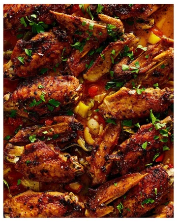 Overhead shot of sizzling, glazed chicken wings glistening with a rich, dark sauce, garnished with fresh herbs on a buffet line.