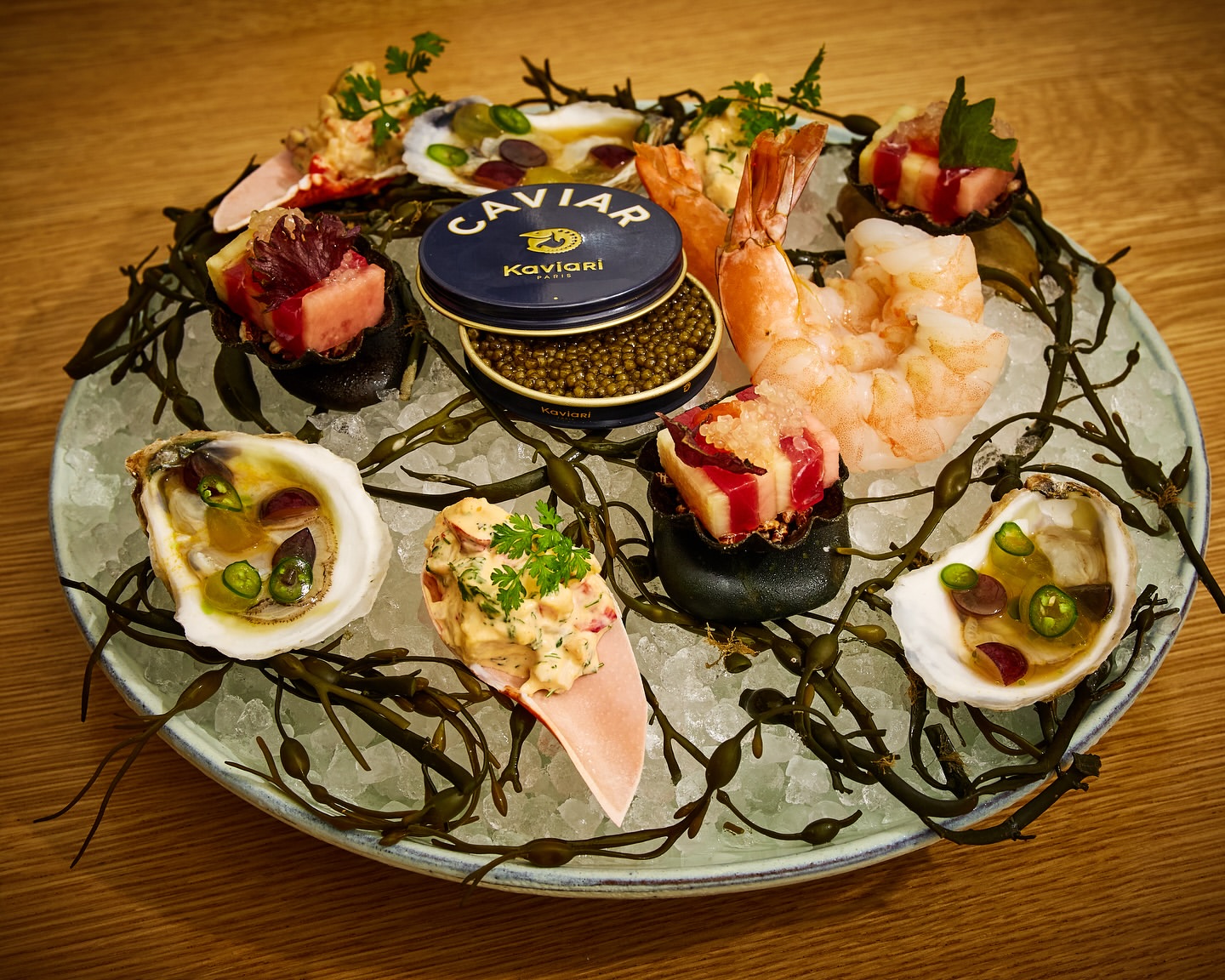 Overhead shot of a seafood platter with oysters, shrimp, tuna, seaweed, ice, and caviar on a wooden table, food photography, overhead view.