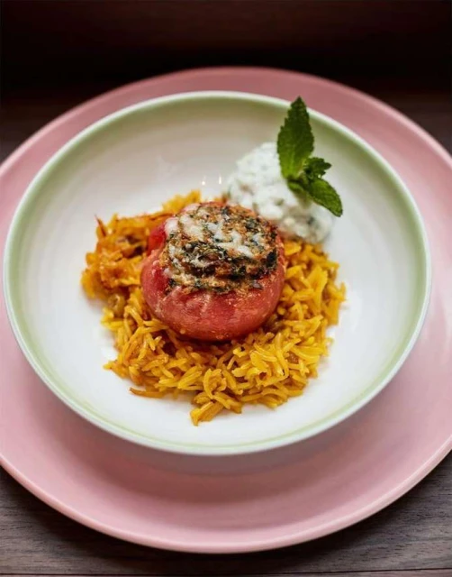Overhead view of a tomato stuffed with greens and rice, plated with mint yogurt sauce. Food photography with vibrant colors.