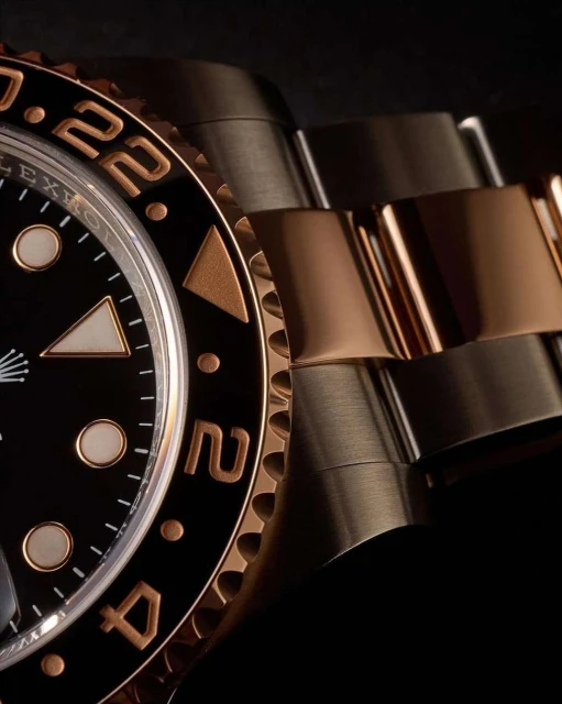 Close-up of a Rolex GMT-Master II watch with a black dial, gold bezel, and two-tone metal band against a dark background.