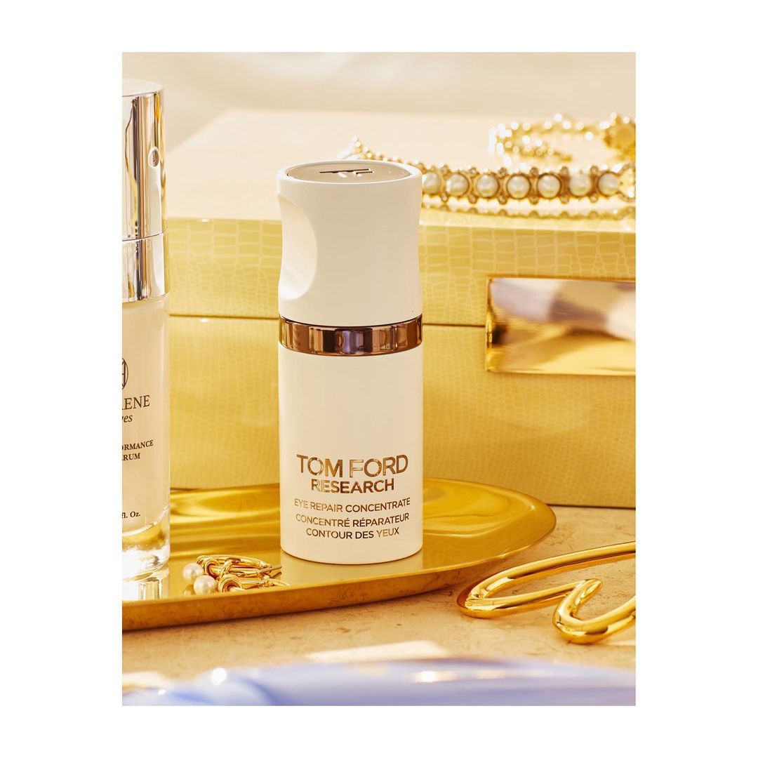 Product shot of Tom Ford eye repair concentrate, and a light colored skin care product with gold accents on a gold surface.