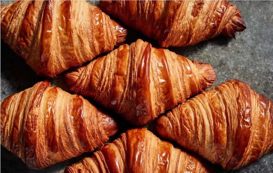 Close-up of golden brown croissants arranged on a dark surface, showcasing their flaky texture and inviting appearance.