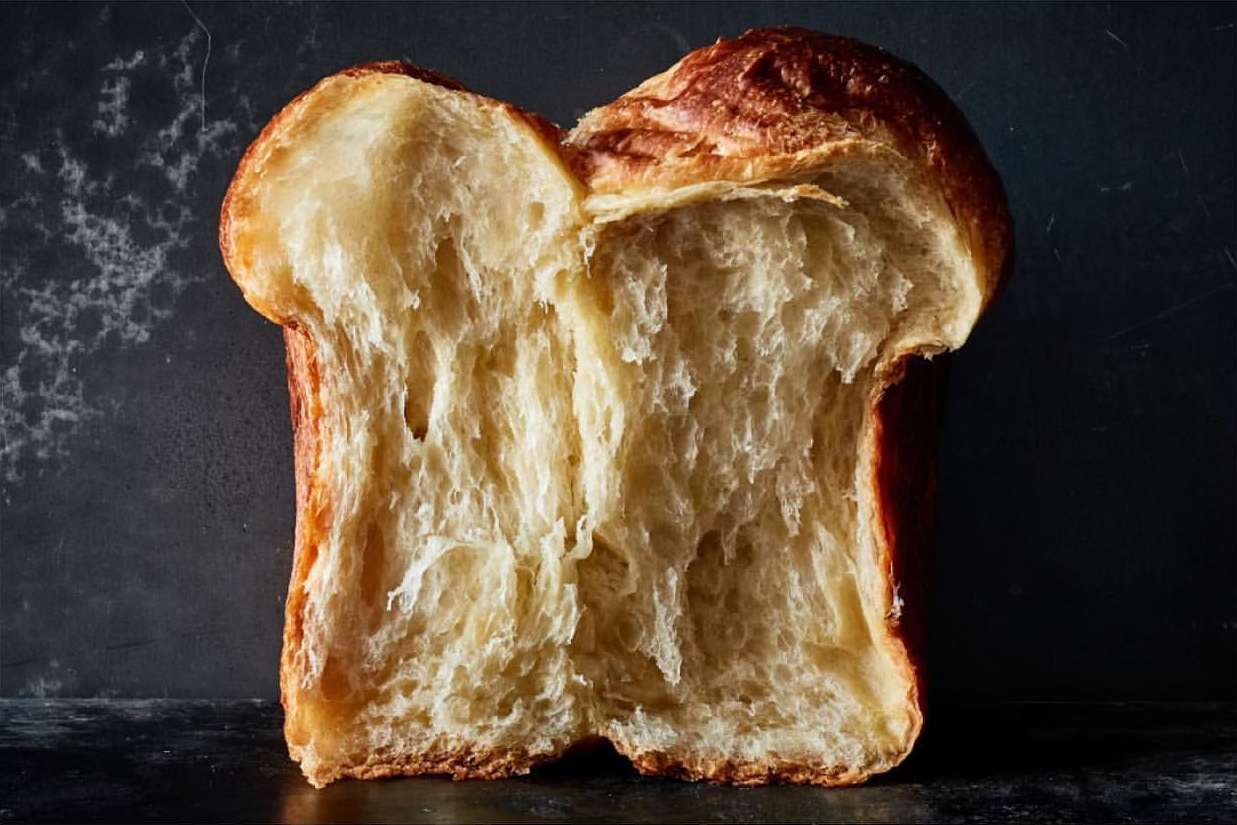 Close-up of a brioche loaf split in half, revealing its soft, airy interior and golden-brown crust against a dark background.
