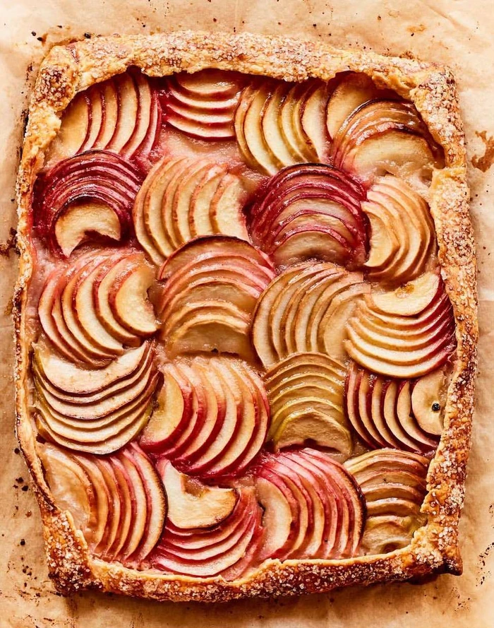 Top-down view of a rectangular apple galette with tightly arranged sliced fruit and a rustic crimped crust on parchment paper.