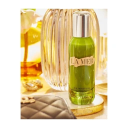 Green La Mer serum bottle standing upright on a round gold tray with a quilted black pouch in the foreground
