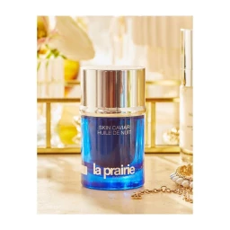 La Prairie Skin Caviar bottle in blue glass with a silver cap resting on a surface with skincare items and flowers.