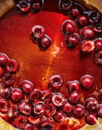 Glossy red cherries submerged in a vibrant amber and crimson caramel syrup inside a copper pot.