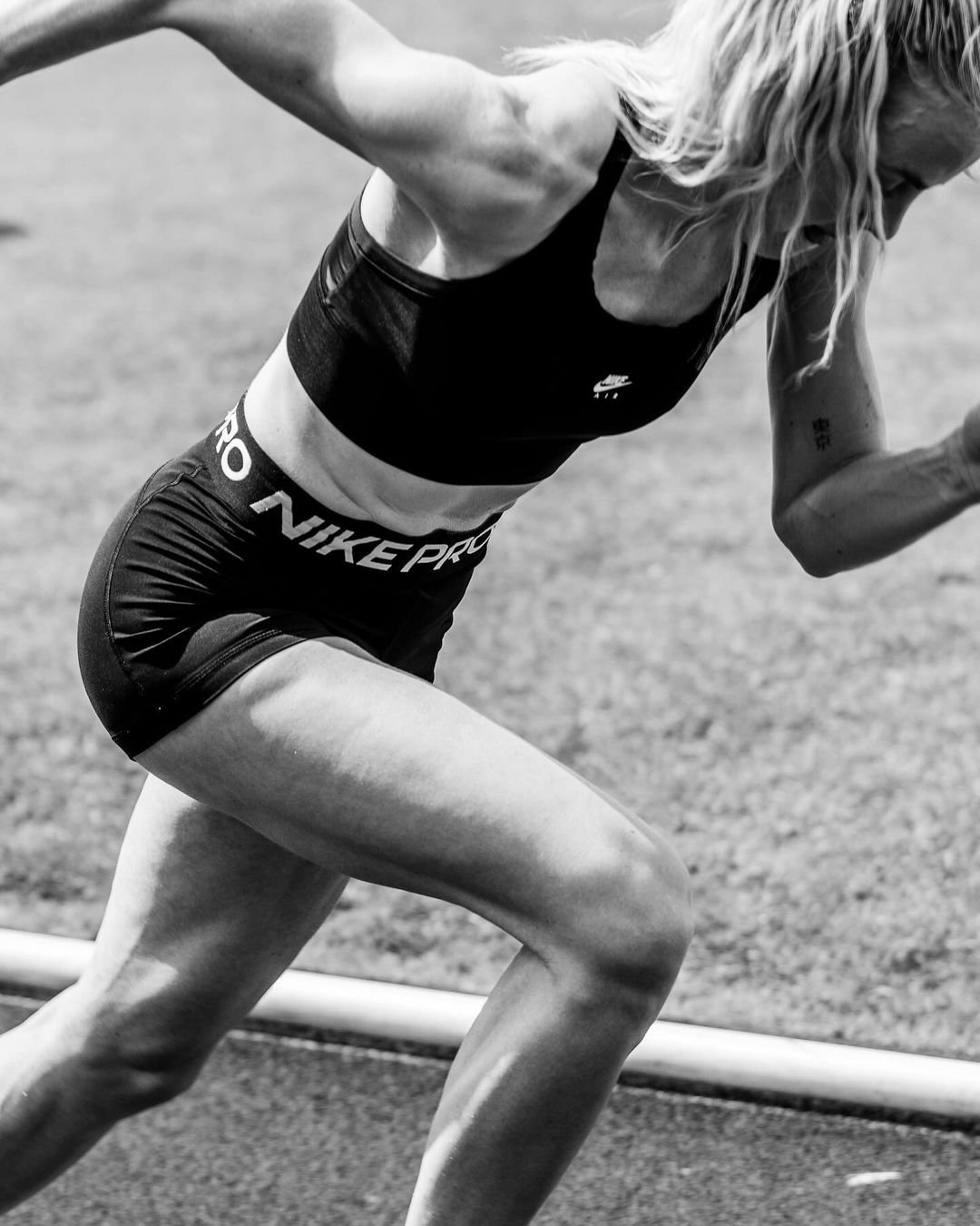 A monochrome image of a female athlete in motion, wearing Nike Pro sportswear, captured in a close-up shot that focuses on her muscular build.