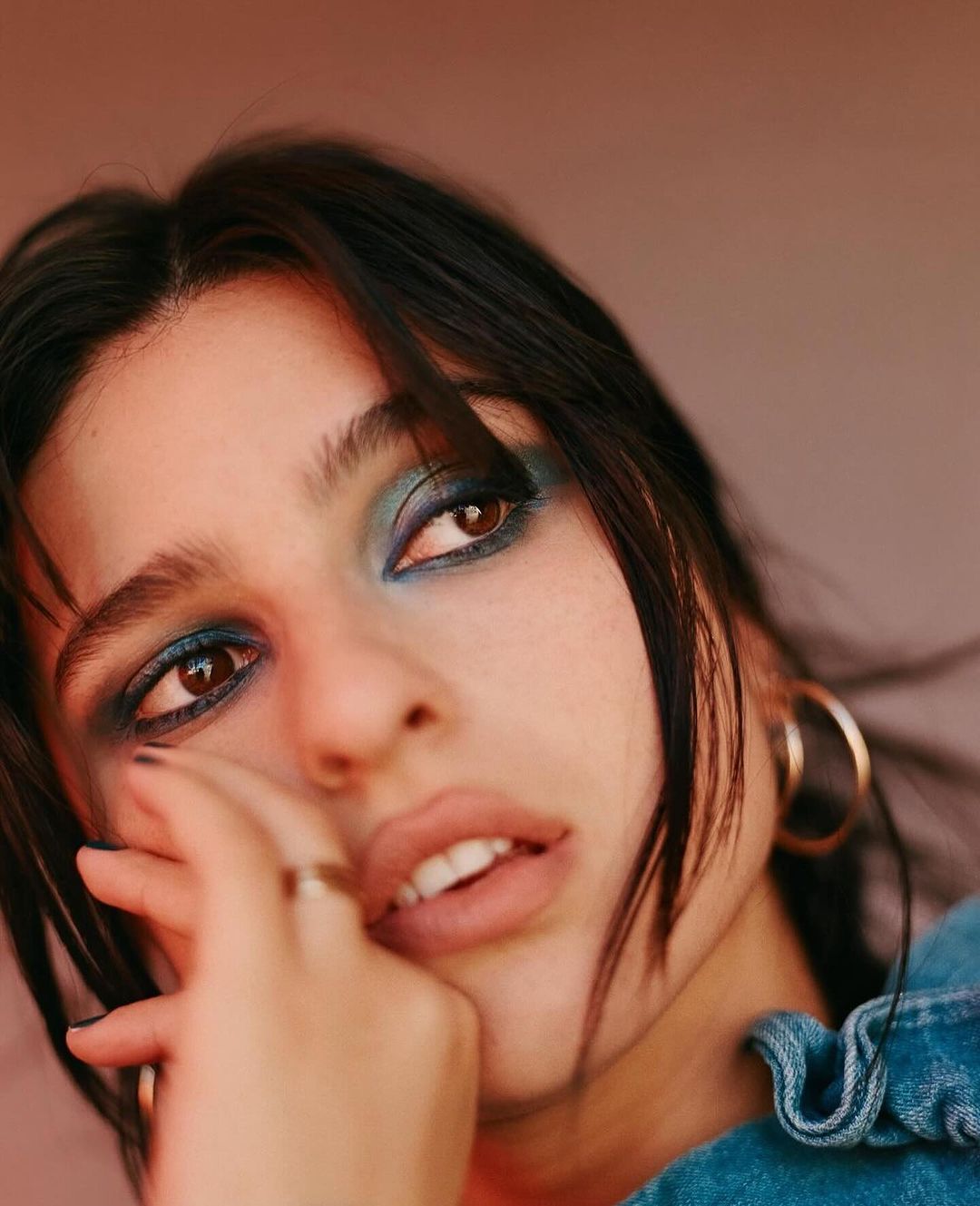 Close up portrait of a young woman with blue eyeshadow, hoop earrings, and denim clothing by photographer Jon Stars.