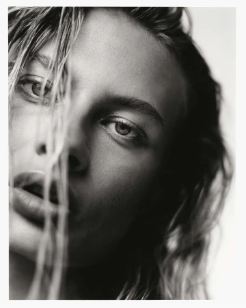 Close-up monochrome portrait of a model with wet hair framing her face against a plain background.