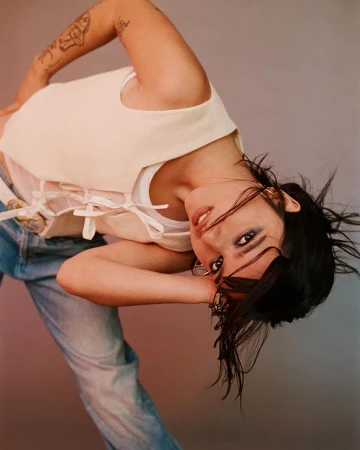 Portrait of a woman wearing a cream vest and blue jeans posing against a grey seamless studio backdrop
