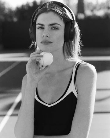Monochrome portrait of a woman wearing over-ear headphones and holding a tennis ball near a tennis court in Los Angeles