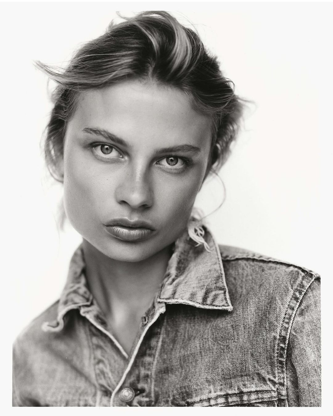 Monochrome portrait of a woman with short hair wearing a denim shirt against a bright background in a studio setting.