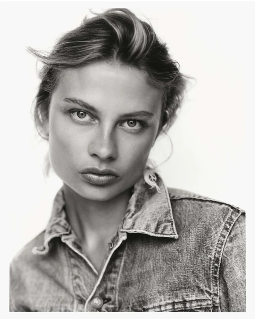 Monochrome portrait of a woman with short hair wearing a denim shirt against a bright background in a studio setting.