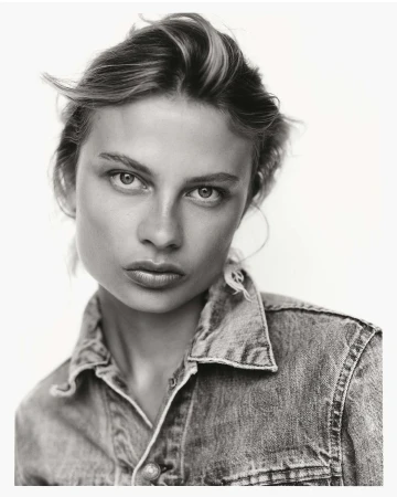 Monochrome portrait of a woman with short hair wearing a denim shirt against a bright background in a studio setting.
