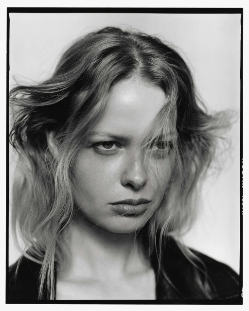 Striking black-and-white portrait of a young woman with blonde hair and a serious expression, wearing a dark leather jacket against a plain background.