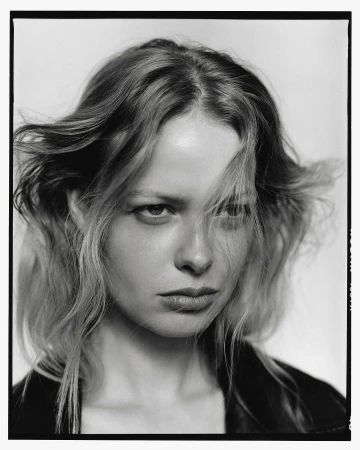 Striking black-and-white portrait of a young woman with blonde hair and a serious expression, wearing a dark leather jacket against a plain background.
