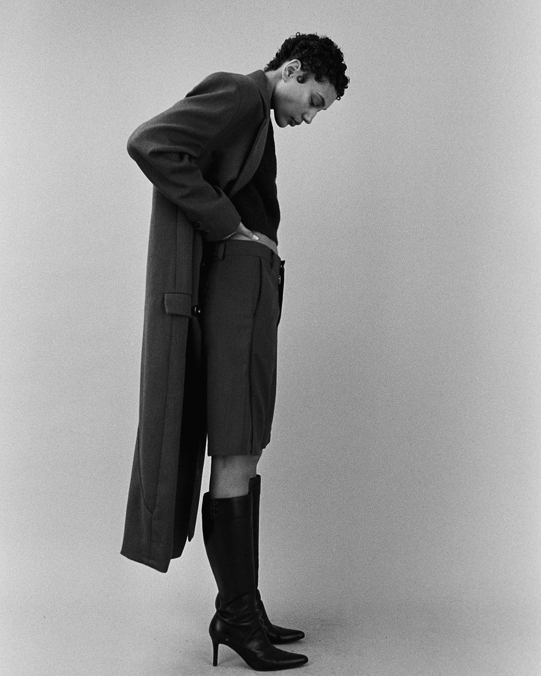 Model wearing a dark long coat and high boots photographed in monochrome by Jon Stars.
