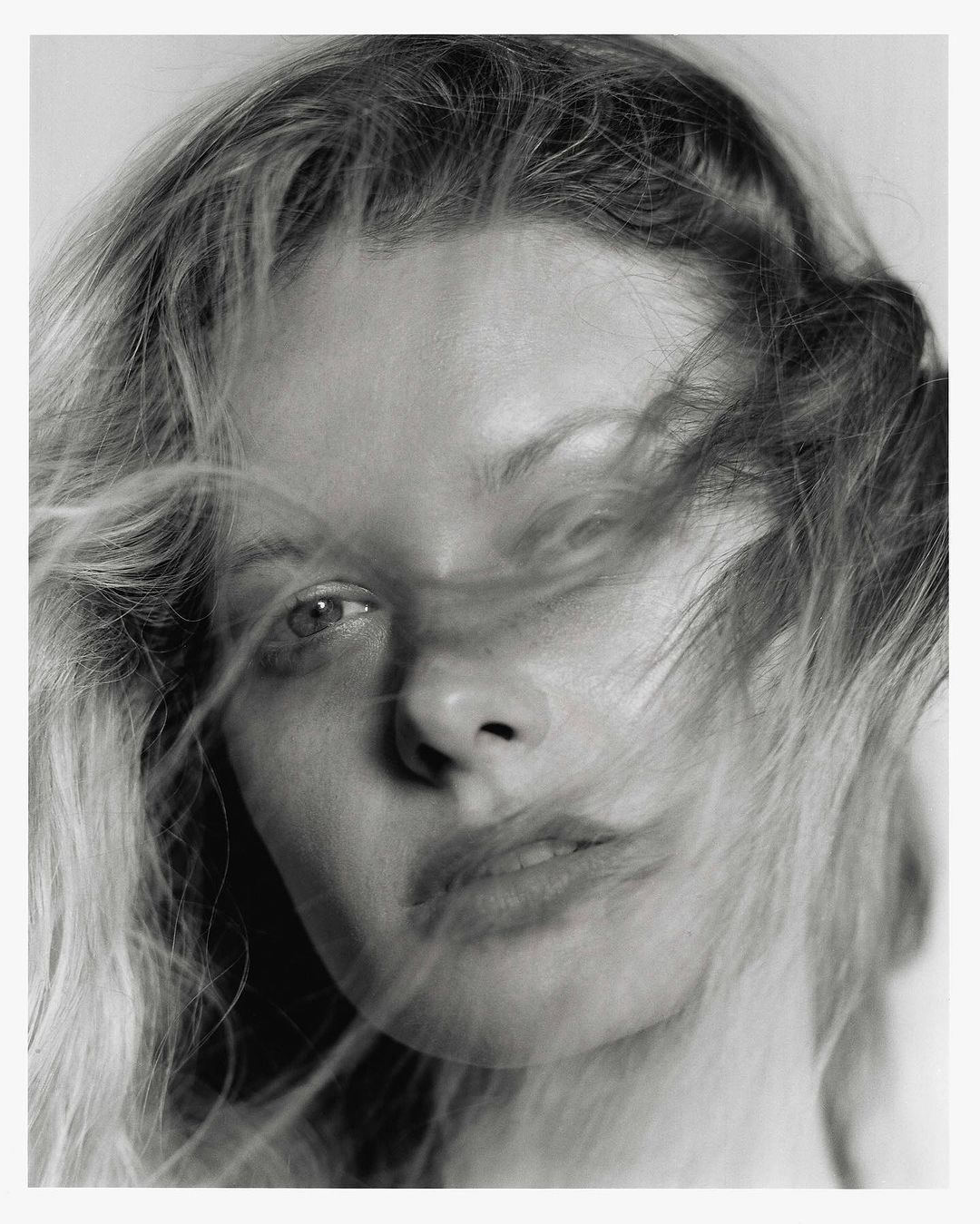 Close-up portrait of a woman with blonde hair blowing across her face photographed by Jon Stars