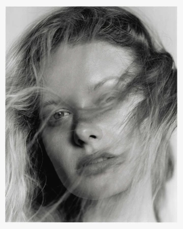 Close-up portrait of a woman with blonde hair blowing across her face photographed by Jon Stars