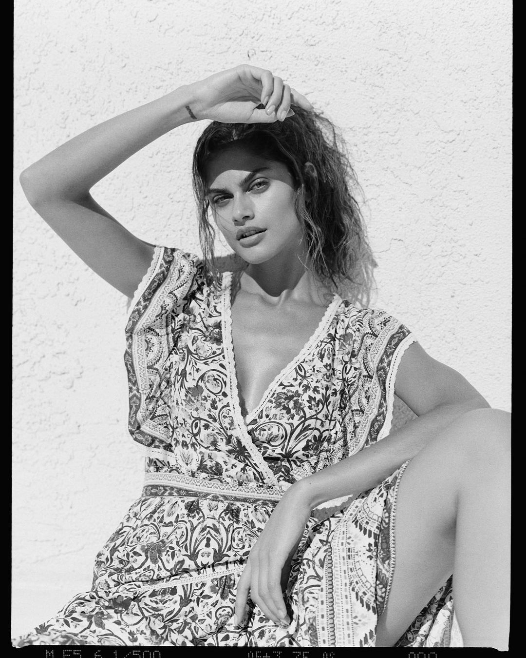 Black and white portrait of a woman in a patterned dress posing against a textured stucco wall in Los Angeles.