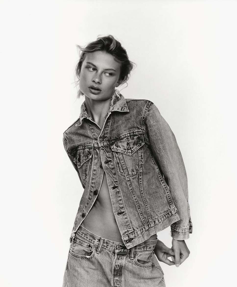 Monochrome portrait of a woman wearing a denim jacket and jeans against a plain white background