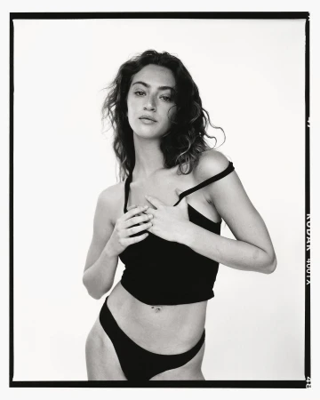Monochrome portrait of a woman in a dark top and underwear, posed in front of a bright background, framed by a black border.