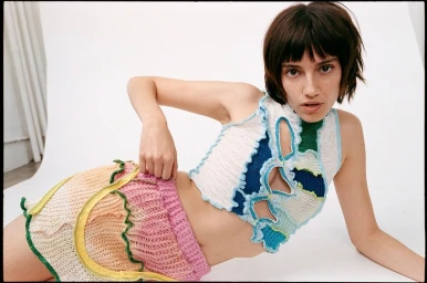 Model with dark bob hair wearing multicolored knit crop top and pink skirt against white seamless studio backdrop
