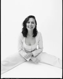 Smiling woman with dark hair wearing a light-coloured matching suit seated against a white background