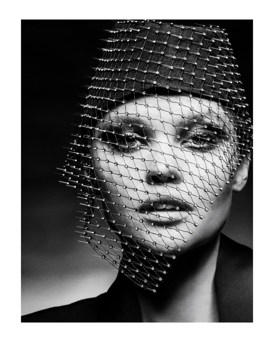 Monochrome portrait of a woman with a beaded veil, wearing a dark jacket, captured in a photo studio with soft, even lighting.